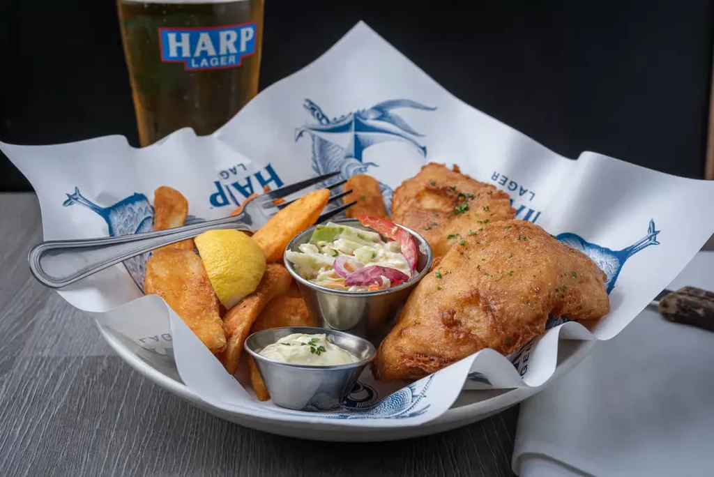 Fish and chips served with coleslaw, tartar sauce, and a Harp Lager.