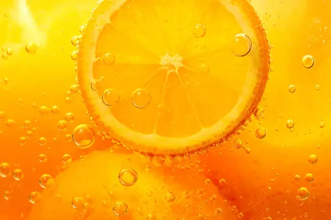 Orange slice submerged in bubbly, orange-colored liquid.