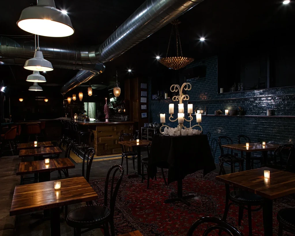 Dimly lit restaurant interior with tables, bar, candelabra, and industrial lighting.
