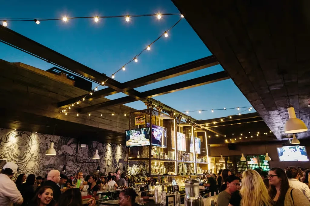 Rooftop bar at dusk with string lights and people socializing.