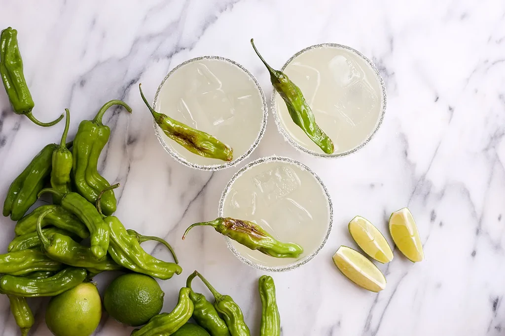 Three lime margaritas, each with a floating green shishito pepper.