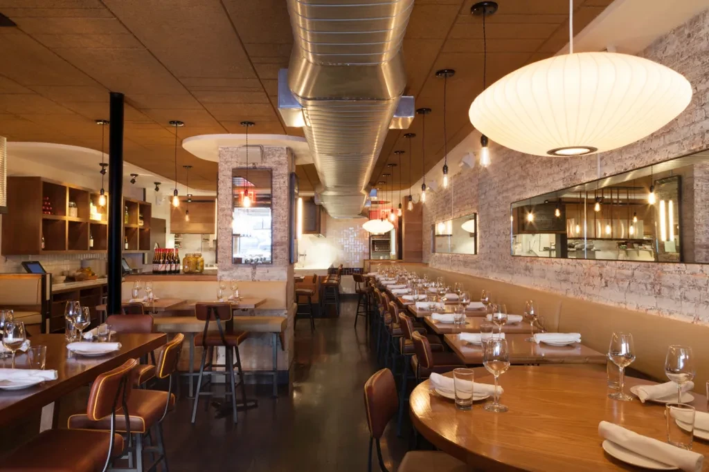Modern restaurant dining area with tables, chairs, and warm lighting.