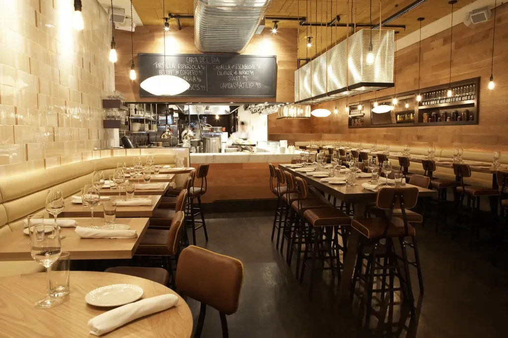 Modern restaurant interior with dining tables, communal seating, and open kitchen.