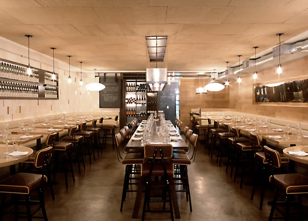Modern restaurant interior with communal table, banquettes, and wine racks.