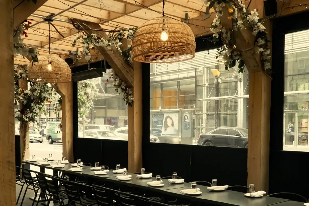 Restaurant patio with long table, warm lighting, and urban view.