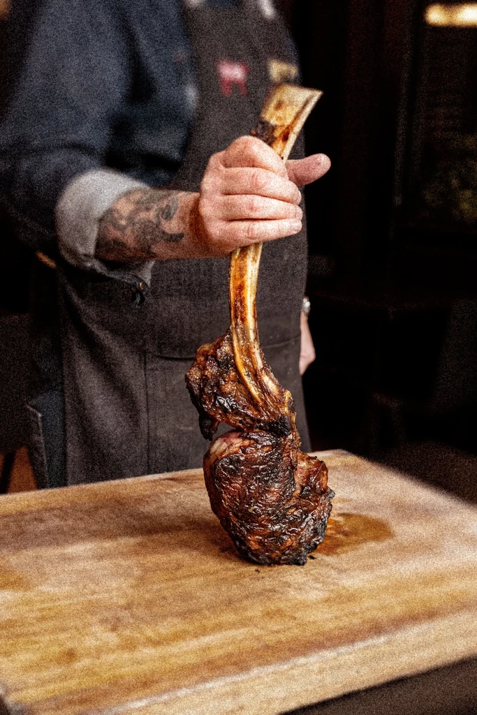 Hand holding an upright, perfectly grilled tomahawk steak with a prominent bone.