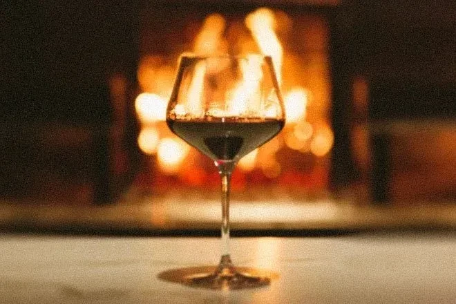 Red wine in a glass, with a blurred fireplace in the background.