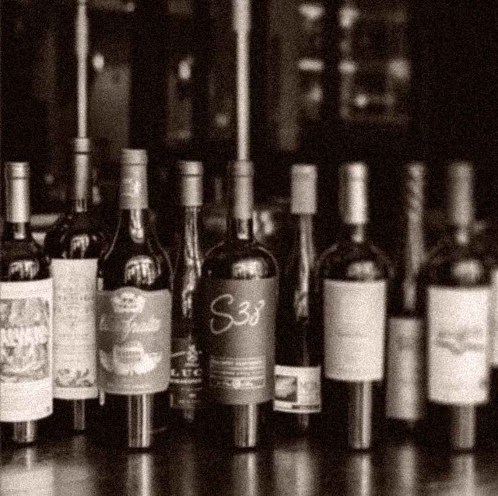 Sepia-toned photo of a collection of wine bottles on a bar.