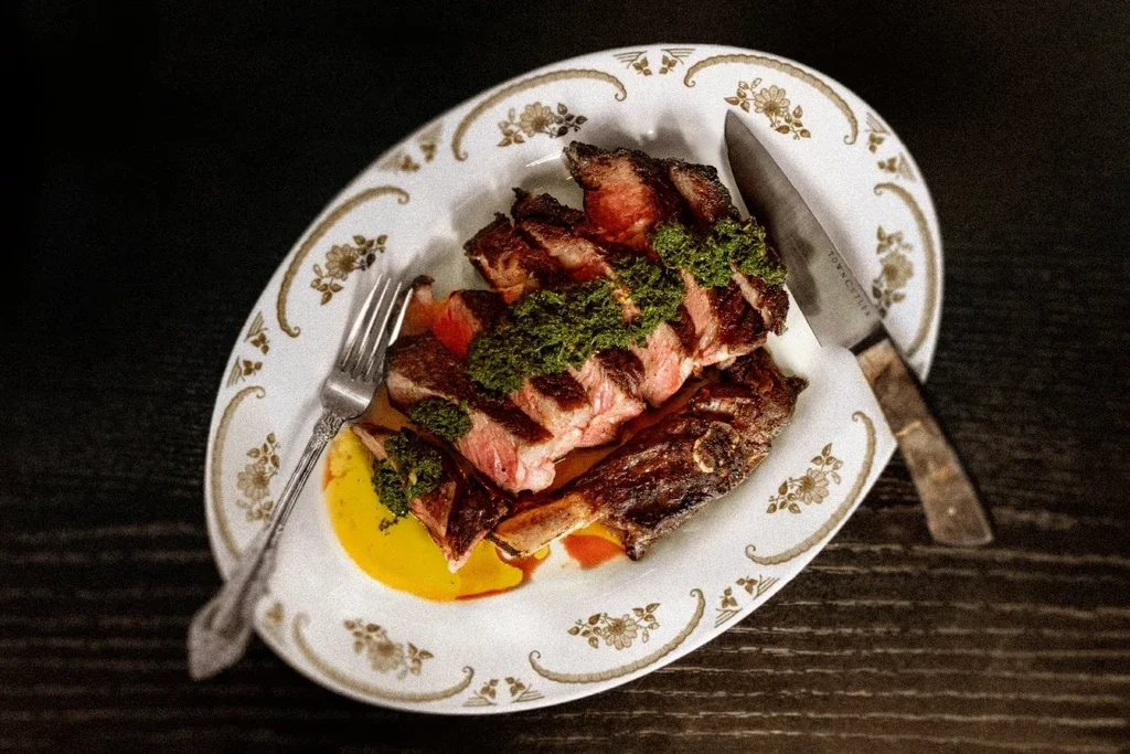 Sliced steak with chimichurri, braised short ribs, and cutlery.