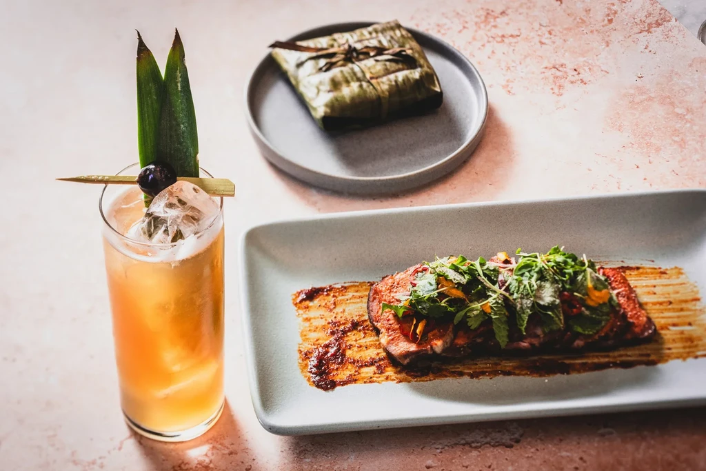 Cocktail, meat dish, and food wrapped in a banana leaf.