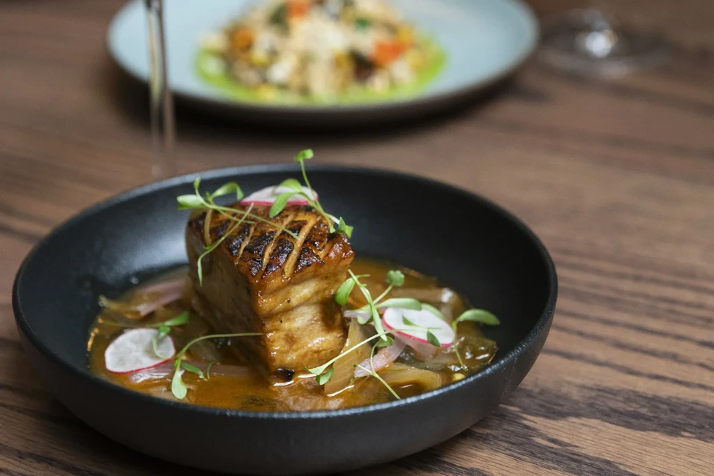Plated pork belly with crispy skin, sauce, radish, and microgreens.