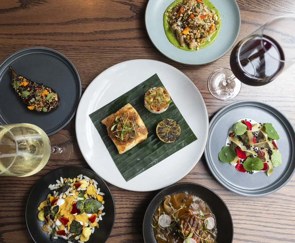 Flat lay of multiple elegantly plated dishes and glasses of wine.