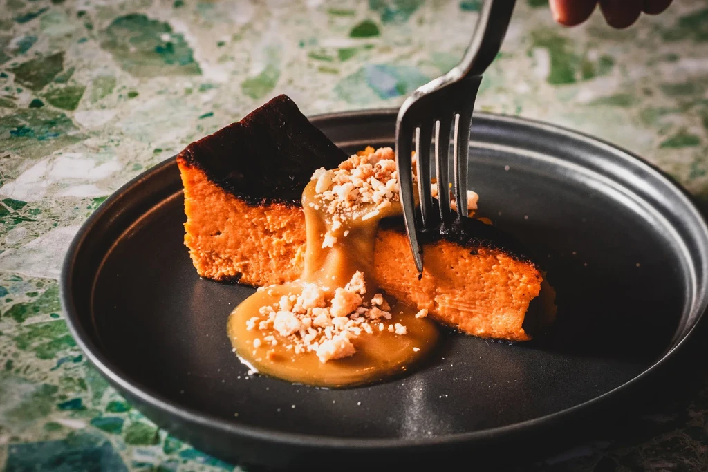 Slice of burnt cheesecake with caramel sauce on a dark plate.