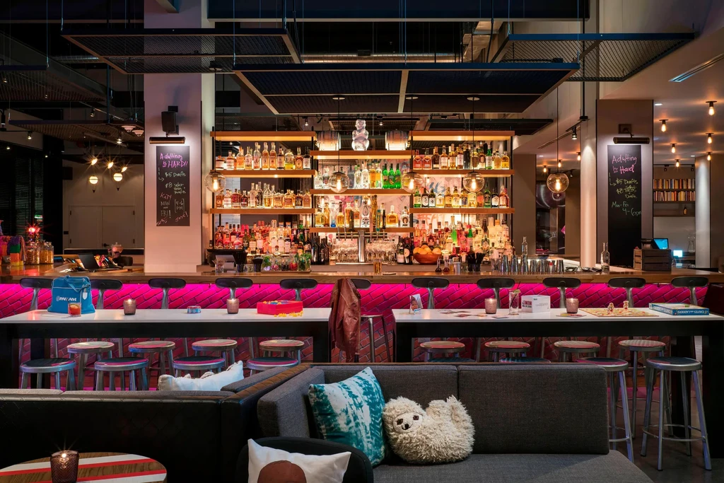 Modern bar with magenta LED lighting, communal table, and seating area.