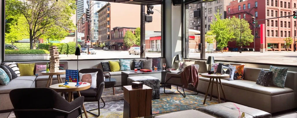 Restaurant interior with colorful seating, games, and drinks by city window.