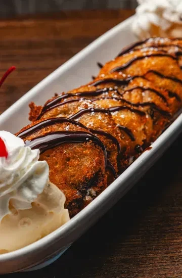 Deep-fried dessert drizzled with chocolate and sugar, with ice cream.
