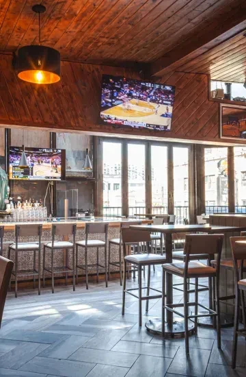 Restaurant interior with a bar, high-top tables, and large windows.