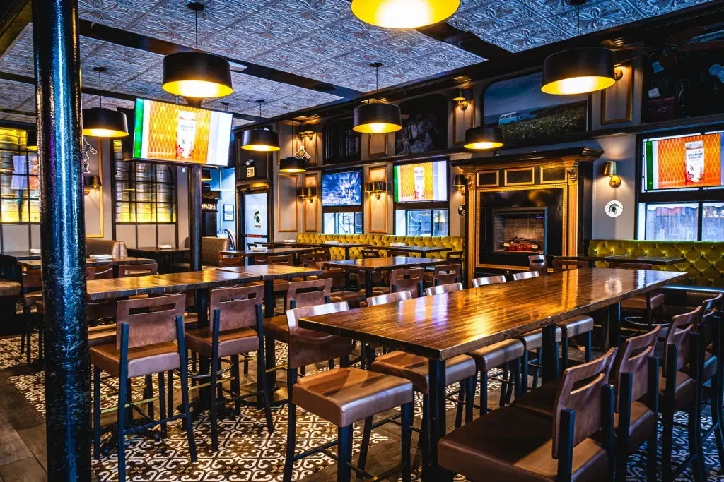 Restaurant interior with high-top tables, booths, patterned ceiling, and TVs.