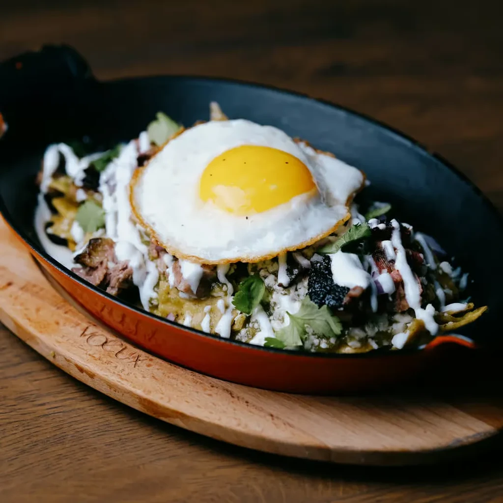 Chilaquiles in a red cast iron skillet on a wooden board.
