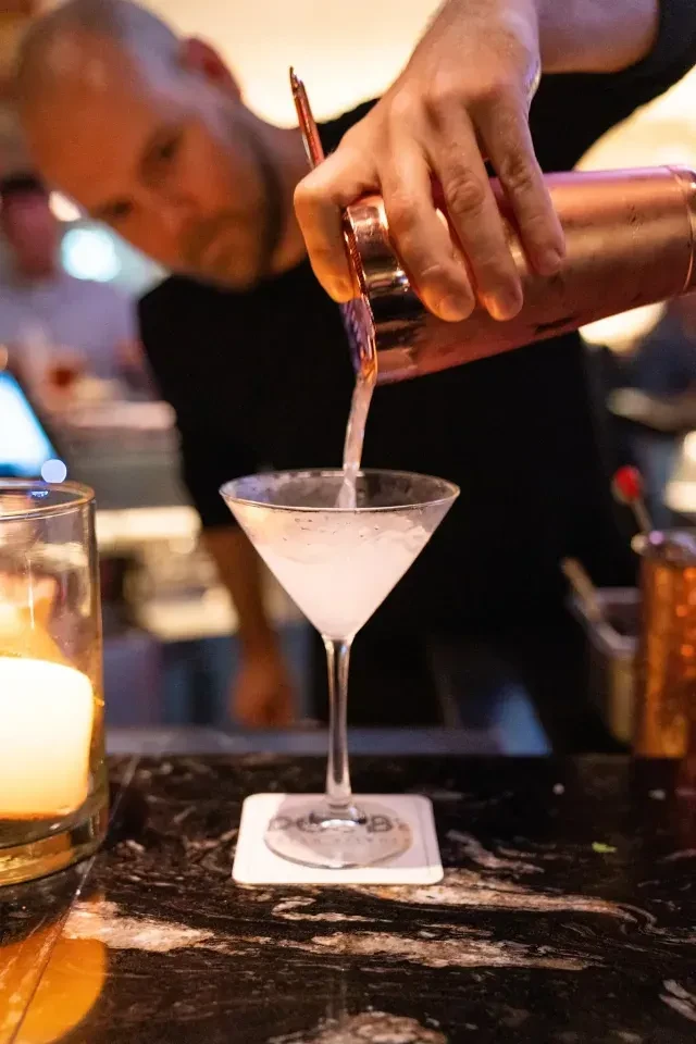 Bartender pours a light-colored cocktail from a copper shaker.
