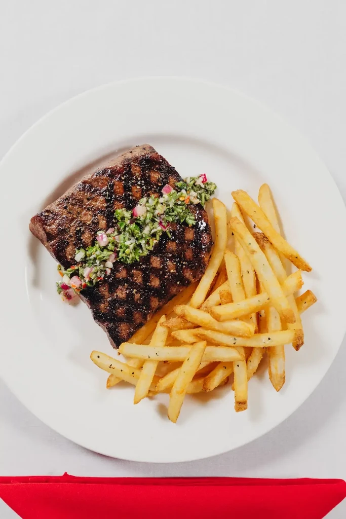 Grilled steak with chimichurri and french fries on a white plate.