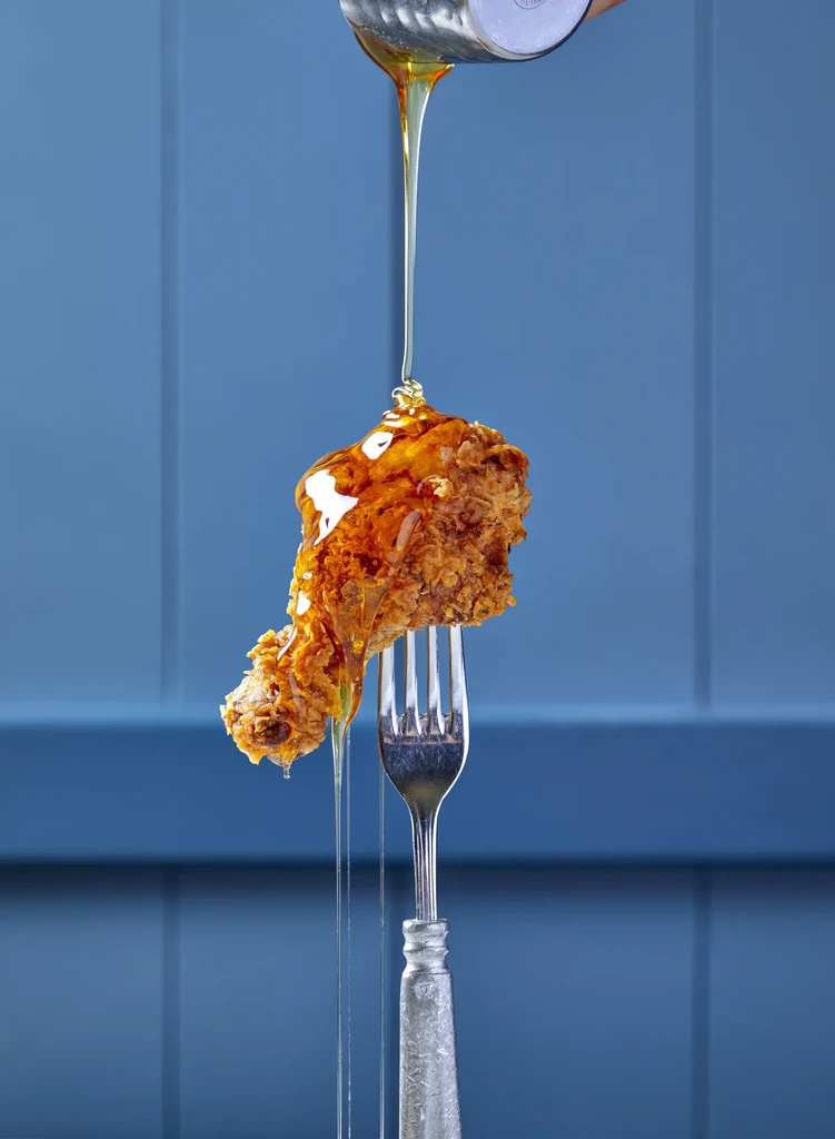 Fried chicken drumstick with honey or syrup being poured over it.