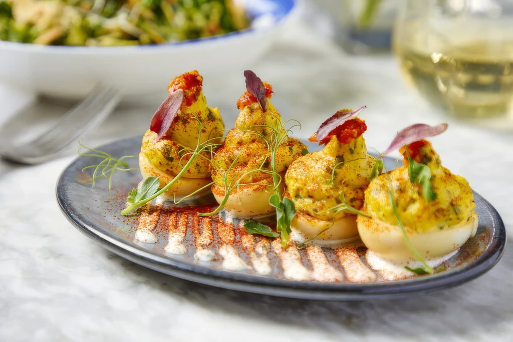 Four deviled eggs garnished with herbs and spice on a speckled plate.