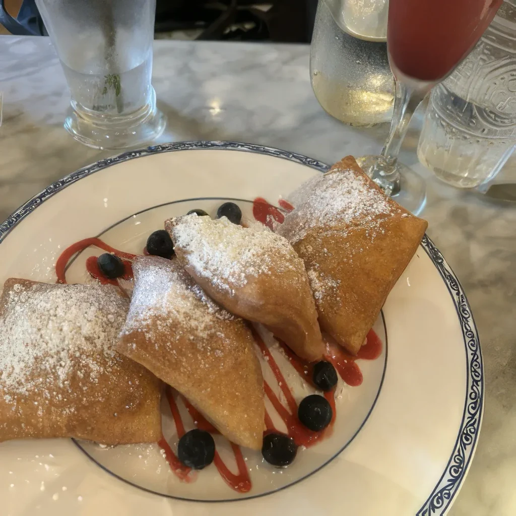 Fried pastries with powdered sugar, berry sauce, and fresh blueberries.