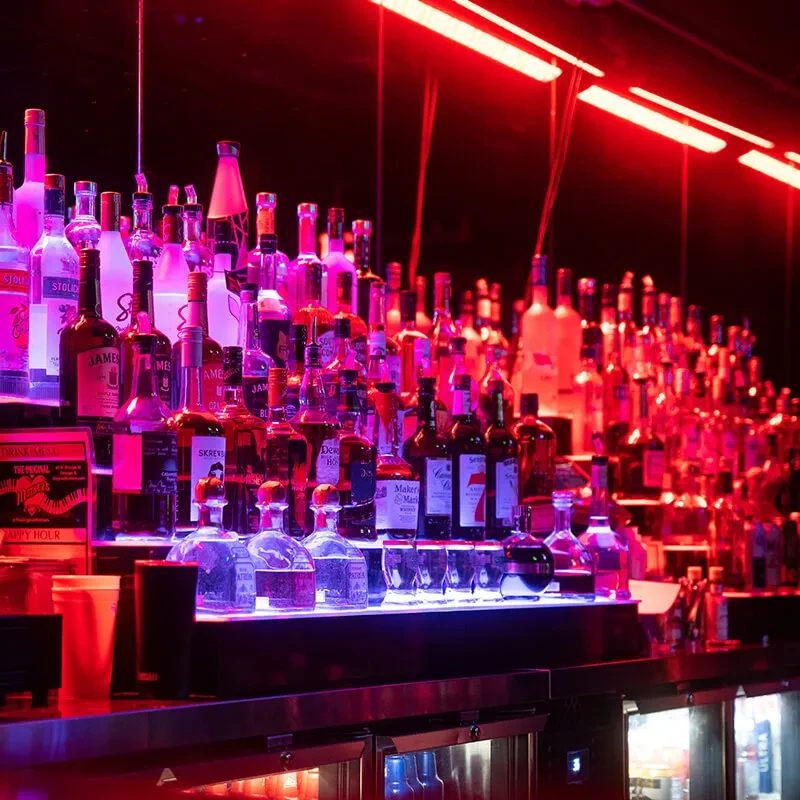 A well-stocked bar with glowing bottles and red neon lights.
