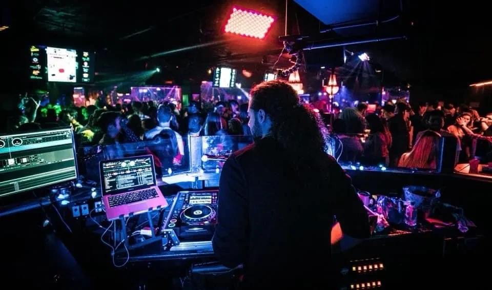 DJ working a multi-screen setup in a dark, vibrant club.