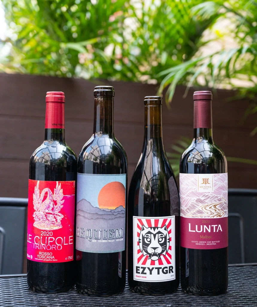 Four bottles of red wine on a dark table, with labels visible.