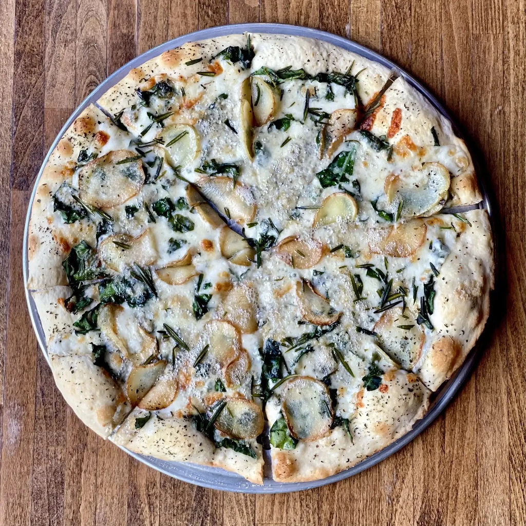 Pizza with potatoes, spinach, cheese, and rosemary on a metal pan.