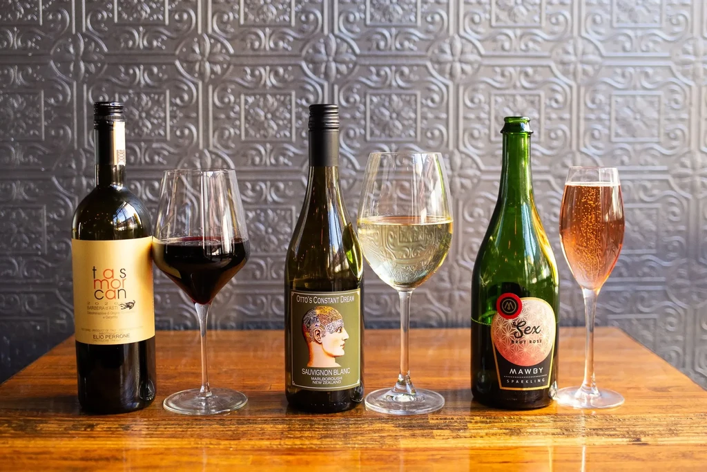 Three bottles of wine and three glasses on a wooden table.