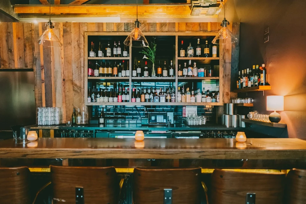 A well-lit bar counter with stools, liquor bottles, and warm lighting.