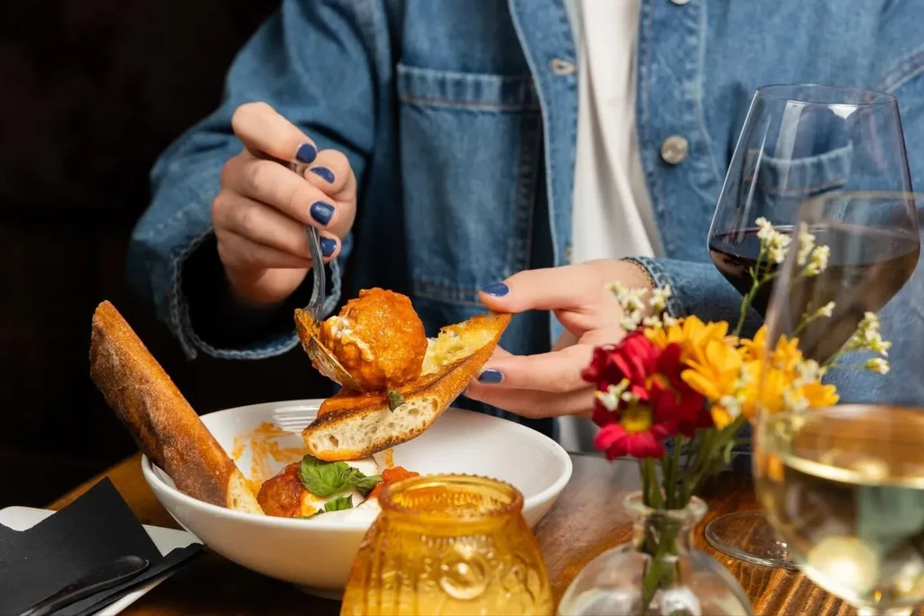 A person lifts a meatball from a dish with toasted baguette.