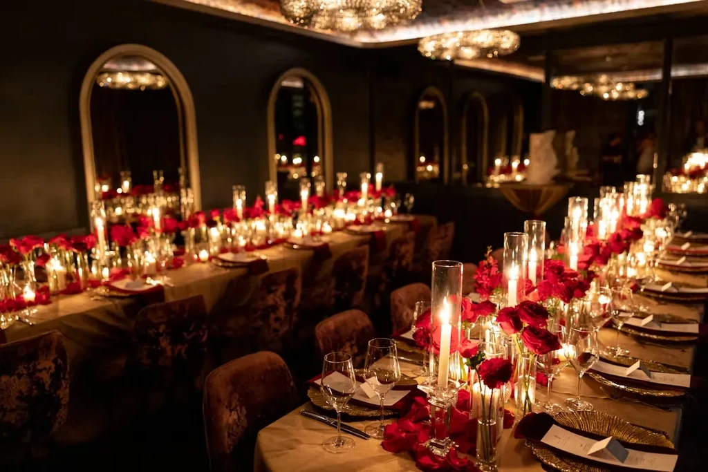 Long dining table set with candles, red roses, and golden chargers.
