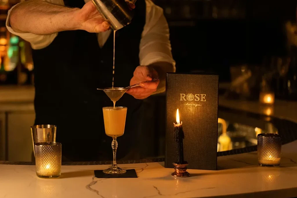Bartender pouring a cocktail from a shaker into a stemmed glass.