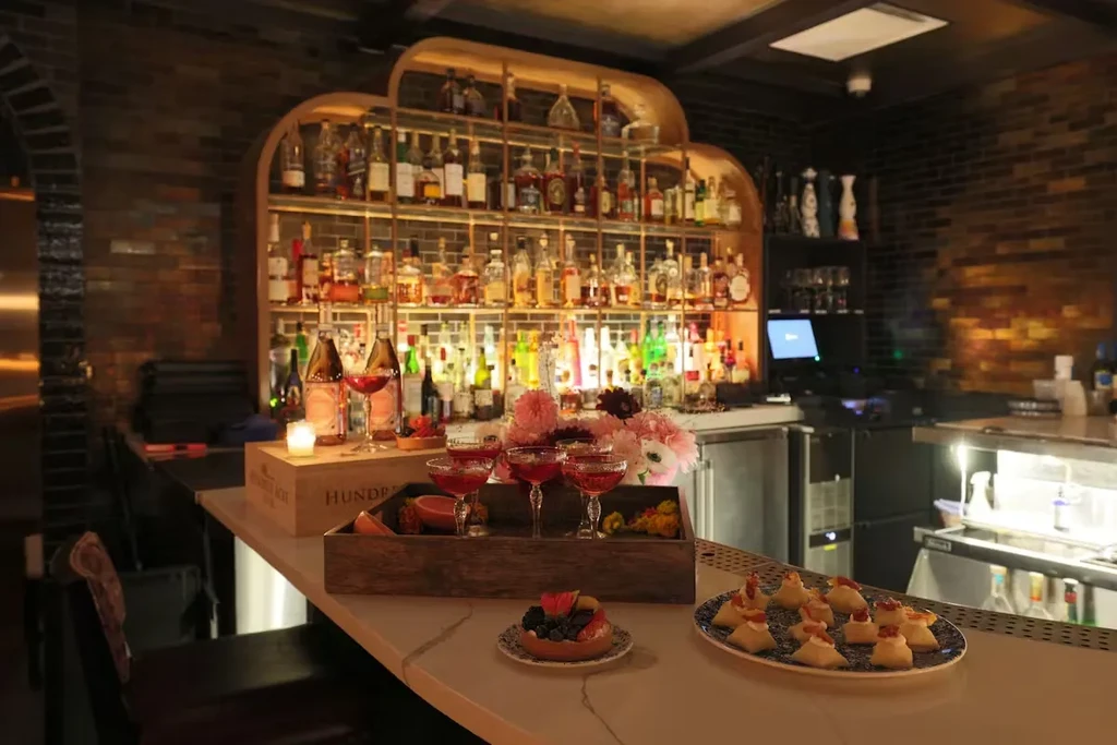 Elaborately stocked bar counter with pink cocktails, tart, and appetizers.