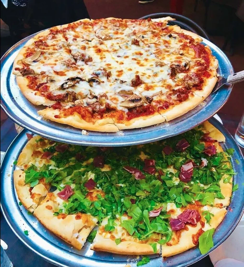 Two pizzas stacked on serving trays, one cheese and one arugula.