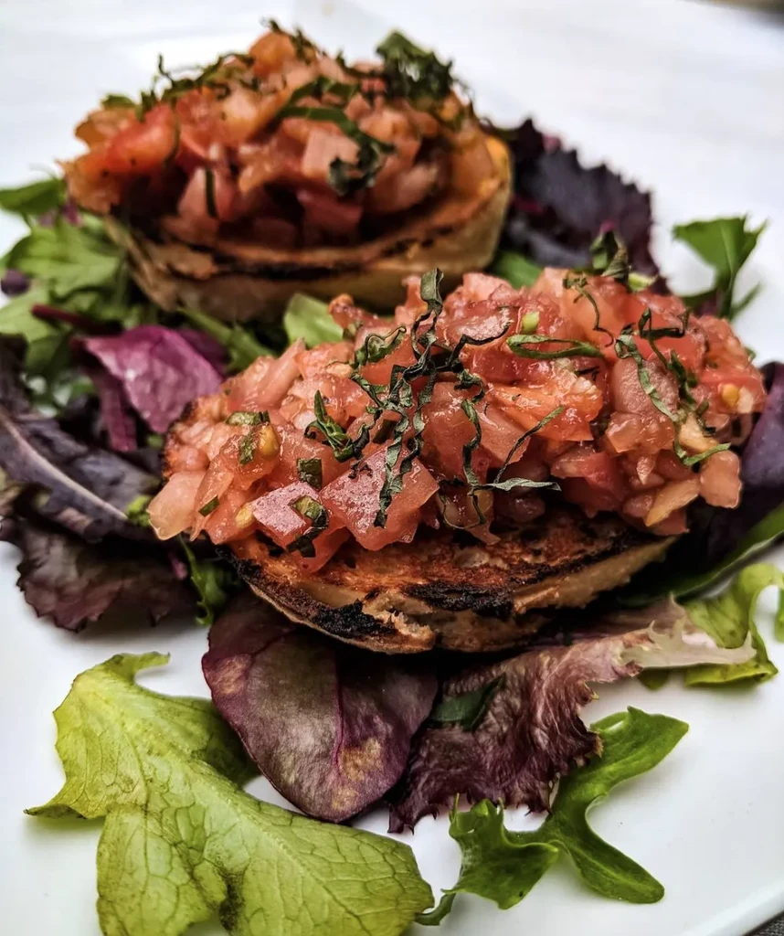 Two servings of bruschetta with tomatoes, herbs, and mixed greens.
