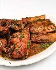 Close-up of roasted chicken and potato wedges with sauce on a plate.