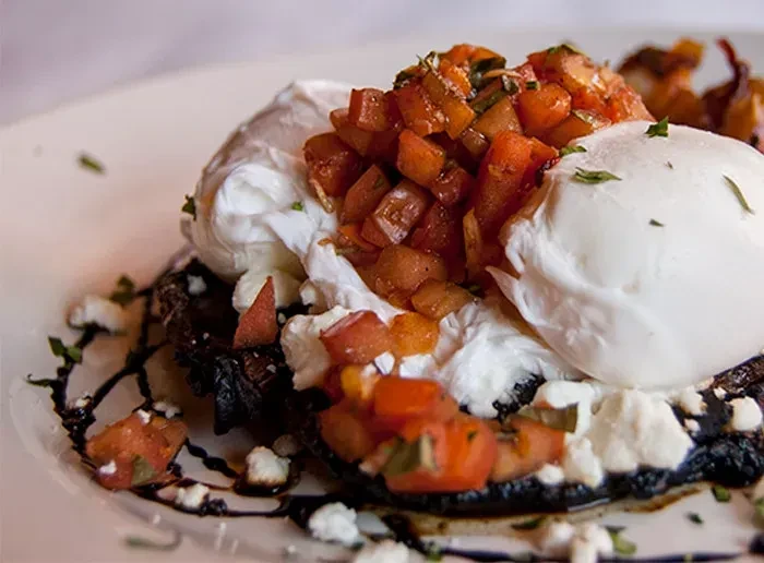 Dark base, creamy topping, tomatoes, and herbs on a white plate.