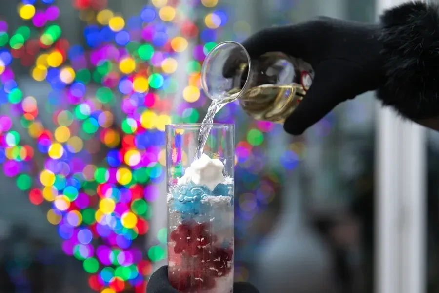Hand in black glove pouring liquid into layered festive drink.