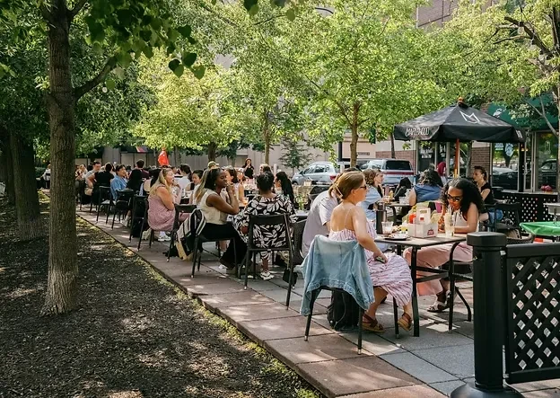 Outdoor restaurant patio filled with people under a canopy of trees.