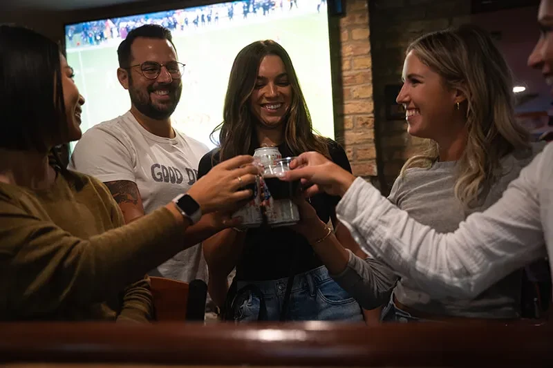 Five people toast with drinks in a dimly lit restaurant.