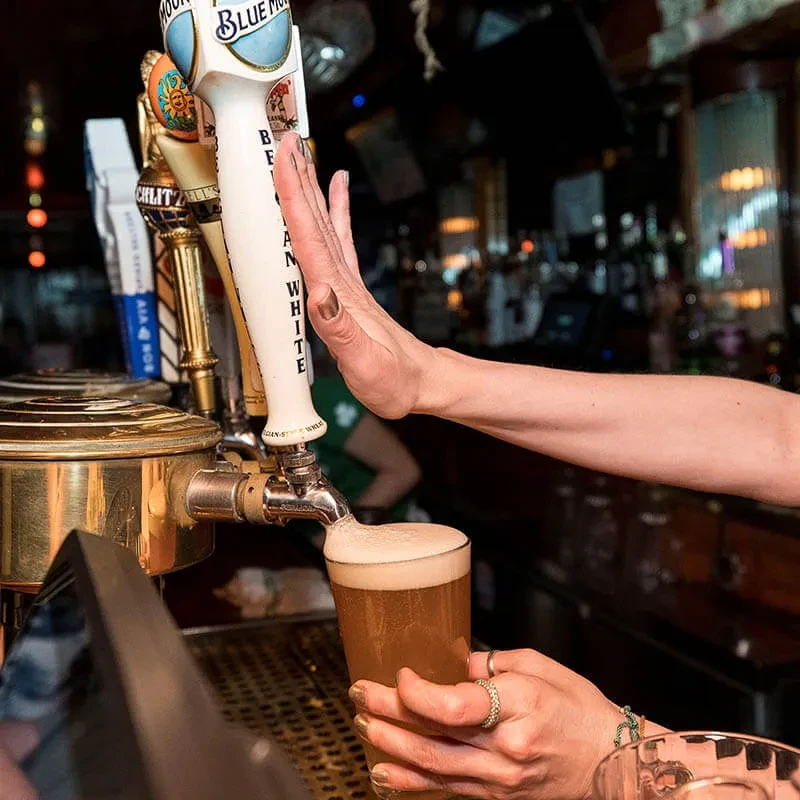 Bartender's hands pouring a Blue Moon White beer from a tap.