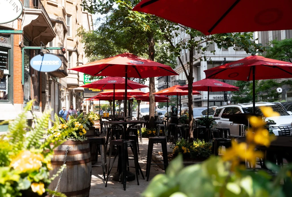 Outdoor restaurant patio with red umbrellas and black tables on a sunny day.