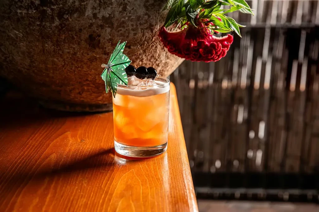 Orange cocktail with berries and umbrella on a wooden surface.