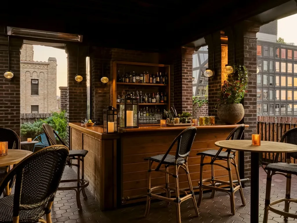 Outdoor bar with wooden counter, shelves, stools, and exposed brick walls.