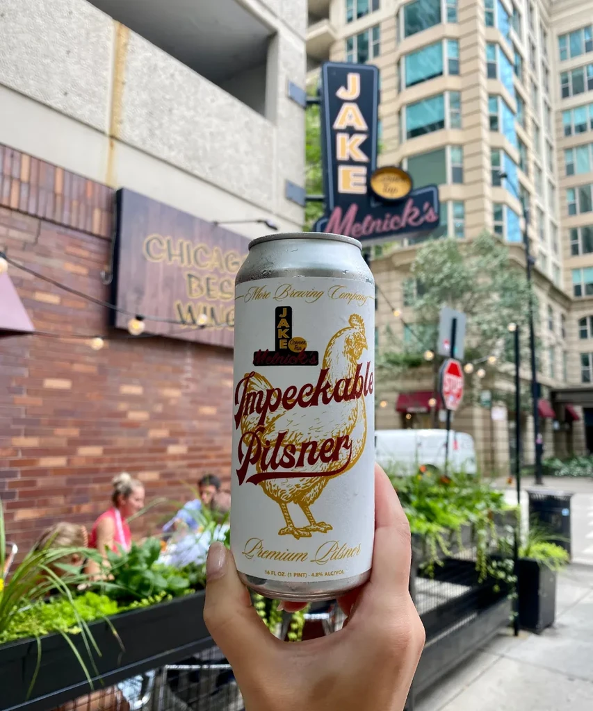 Hand holds a "Impeckable Pilsner" can at an outdoor restaurant.